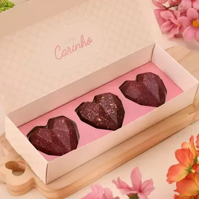 caixa com três bombons em forma de coração castanho-escuro com detalhes dourados