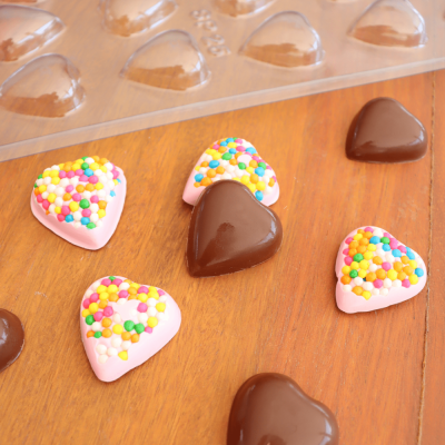 Bombons em forma de coração com cobertura de chocolate e confeitos coloridos sobre madeira