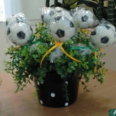 Arranjo decorativo com bolas de futebol em vaso preto e folhagem verde