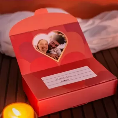 Embalagem vermelha aberta com fotografia de casal e texto amoroso à vista.