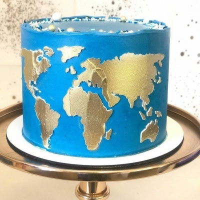 Bolo com mapa mundial dourado em glacê azul e pérolas brancas num suporte metálico.