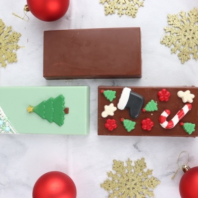 Barras de chocolate natalinas com decorações festivas rodeadas por enfeites vermelhos e dourados
