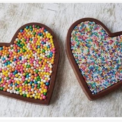 Dois chocolates em forma de coração cobertos por bolinhas coloridas sobre fundo claro