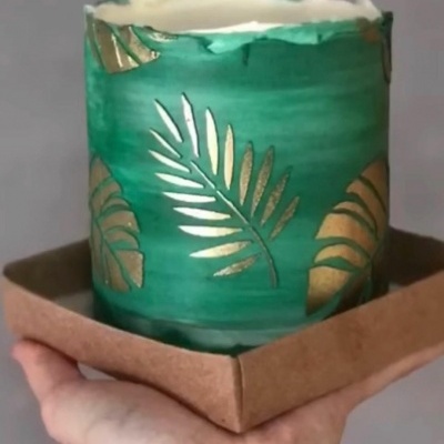 Vela decorativa verde com folhas douradas em suporte castanho