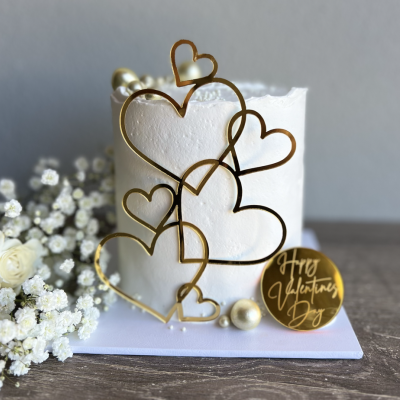 Bolo branco decorado com corações dourados e placa 'Happy Valentine's Day'