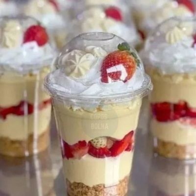 Doce em copo transparente com creme, morangos, chantilly e merengues