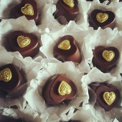 Bombons de chocolate em forma de coração com corações dourados decorativos em papel branco