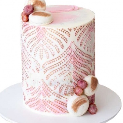 Bolo decorado com creme branco e rosa com padrão dourado, macarons e frutas vermelhas sobre prato branco