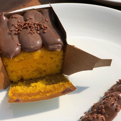 Cupcake amarelo com cobertura e granulados de chocolate, parcialmente embrulhado em papel castanho