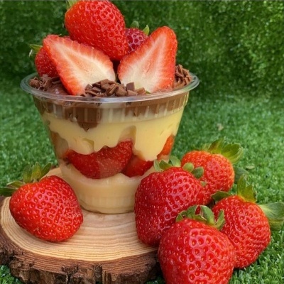 Sobremesa com morangos em copo transparente sobre base de madeira e morangos frescos