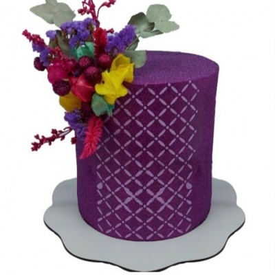 Bolo decorado roxo com padrão geométrico e flores artificiais coloridas no topo