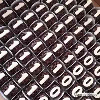 Brigadeiros com cobertura de granulado preto e letras brancas organizados em embalagens brancas