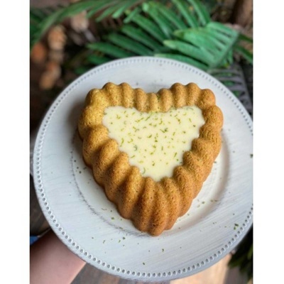 Bolo em forma de coração com creme branco no centro e decoração de raspas verdes num prato branco.