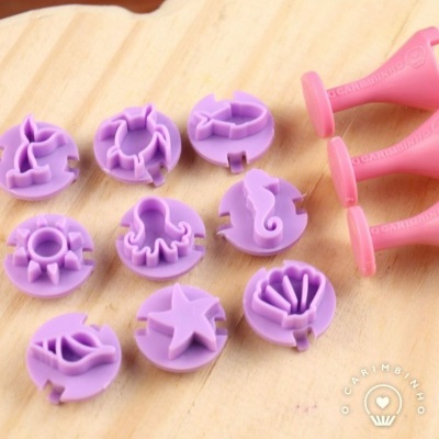 Discos de plástico lilás com formas decorativas e aplicadores rosa sobre madeira clara
