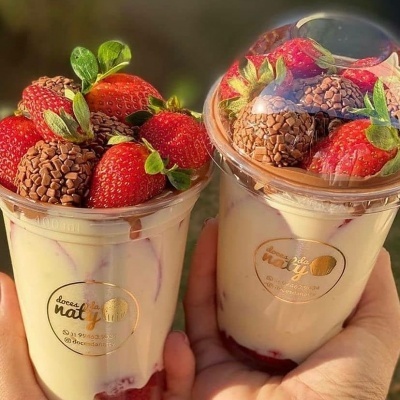 Sobremesas cremosas com morangos e brigadeiros em copos transparentes com tampa em forma de cúpula.