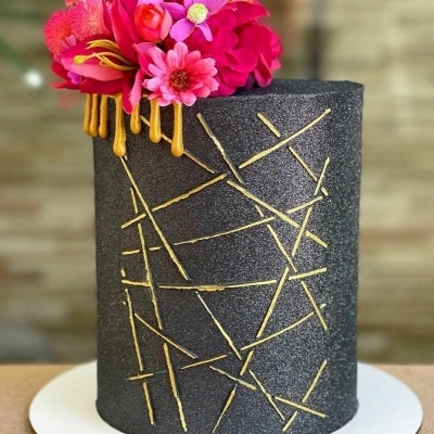 Bolo preto texturizado com decoração dourada e flores rosas no topo