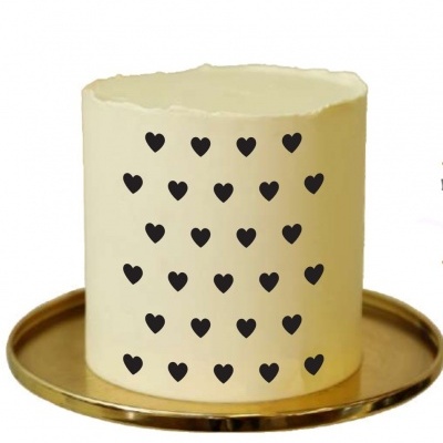 Bolo branco decorado com pequenos corações pretos em fila, numa base dourada