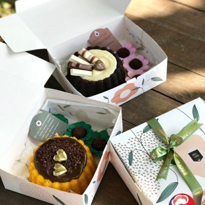 Três caixas decorativas abertas com bolos decorados e cartão da Loja Doce Tentação