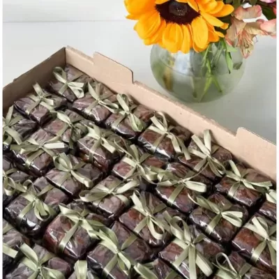 Caixa com chocolates embrulhados em papel castanho e fita dourada, com vaso de flor girassol ao lado
