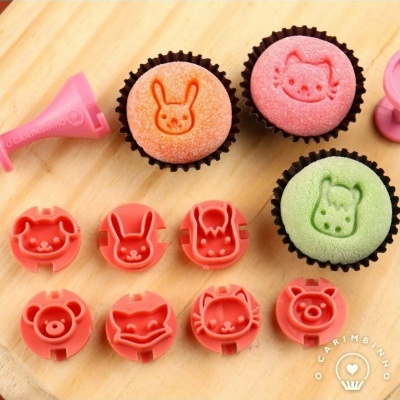 Três cupcakes com carimbos de animais e diversos carimbos de silicone rosa numa superfície de madeira.