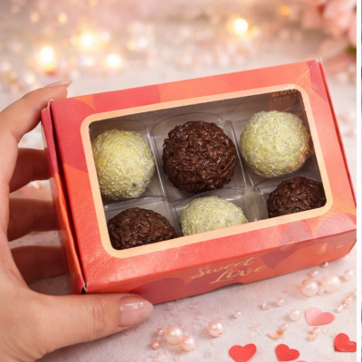 Caixa vermelha com bombons brancos e castanhos em ambiente decorado com pérolas e corações.