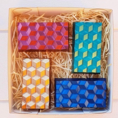 Conjunto de quatro sabonetes geométricos coloridos numa caixa.