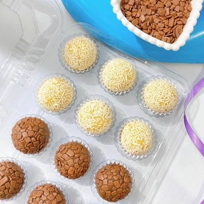Caixa com brigadeiros de granulado castanho e branco e prato azul com recipiente de coração branco com granulado castanho