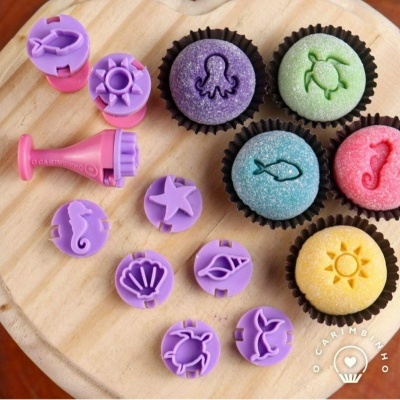 Conjunto de carimbos e bolos coloridos decorados com desenhos marinhos numa tábua de madeira.