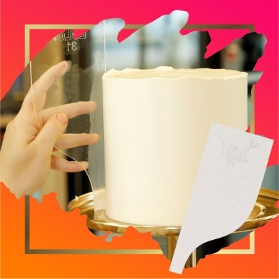 Bolo branco coberto com cobertura lisa sobre prato dourado com mão segurando fita decorativa transparente