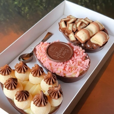 Três ovos de Páscoa decorativos em caixa branca com diferentes coberturas e decoração em chocolate.