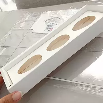 Caixa branca retangular com três janelas ovais mostrando produto fino bege