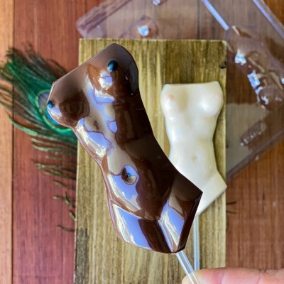 Pirulitos em forma de torso humano em chocolate escuro e branco sobre suporte de madeira.