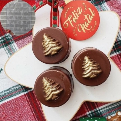 Doces redondos de chocolate decorados com árvores de Natal douradas sobre prato estrela e bola vermelha com texto Feliz Natal