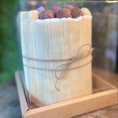 Bolo decorado com frutos secos e embalagem transparente sobre caixa de cartão.