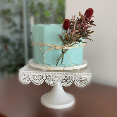 bolo azul claro com fita e flores secas num suporte branco decorativo