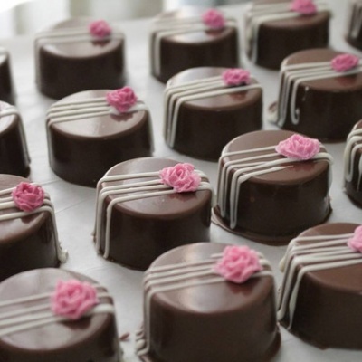 Pequenos bolos redondos cobertos de chocolate com decoração branca e flor cor-de-rosa