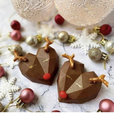 Duas decorações natalícias em chocolate em forma de rena com bolas e flocos de neve ao redor