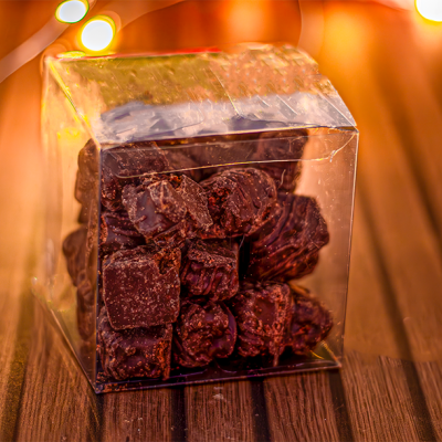 Cubos de chocolate em embalagem transparente sobre superfície de madeira com luzes decorativas.