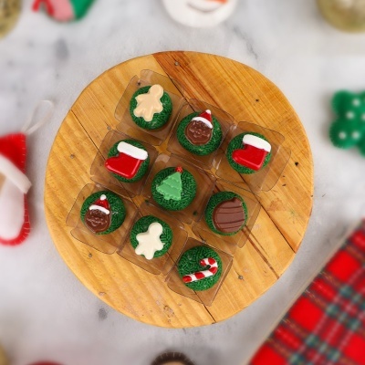 Dez cupcakes natalícios decorados com glacê verde e emblemas coloridos sobre prato de madeira redondo