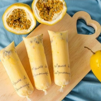 Pacotes de mousse de maracujá em plástico sobre tábua de madeira clara com maracujá ao lado