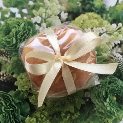 Produto arredondado cor salmão com fita de cetim creme sobre flores verdes