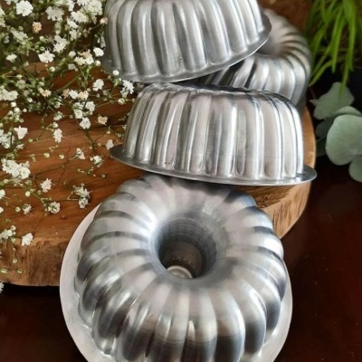 Formas de metal prateado para bolo com design canelado em mesa de madeira com flores brancas