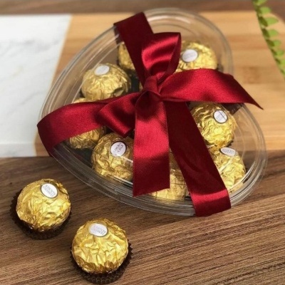 Caixa de bombons em forma de coração com fita vermelha e bombons dourados