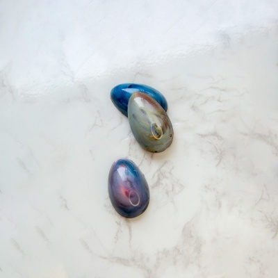 Três pedras decorativas ovais coloridas sobre superfície branca