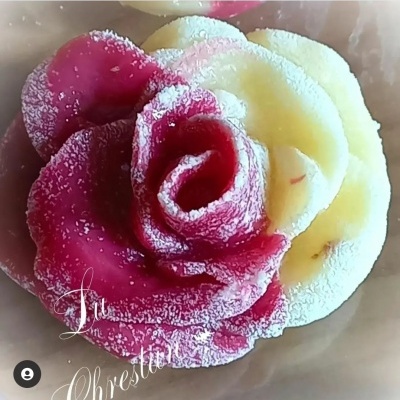 Flor decorativa em forma de rosa com pétalas rosa escuro e amarelo claro polvilhadas com pó branco