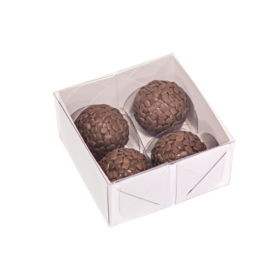 Quatro brigadeiros cobertos com lascas de chocolate numa caixa branca com tampa transparente