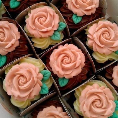 Cupcakes decorados com rosa cor-de-rosa e folhas verdes em caixas brancas
