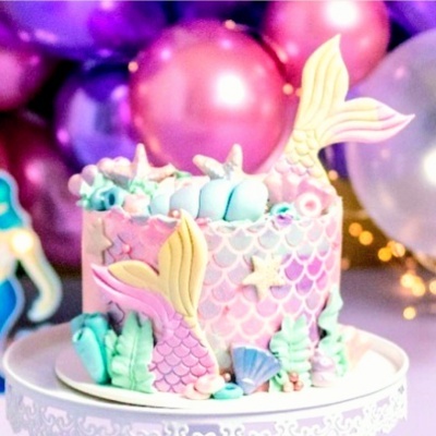 Bolo decorado com tema de sereia em tons rosa e azul com balões ao fundo