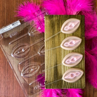 chocolates em forma de lábios sobre tábua de madeira com penas cor-de-rosa ao fundo
