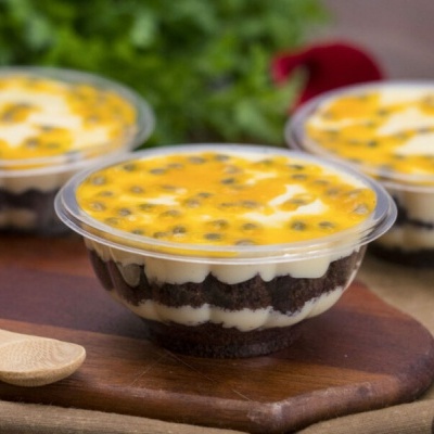 Três tigelas de sobremesa com maracujá em camadas sobre tábua de madeira e pano.